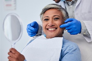 Woman smiling while holding small mirror with dentist